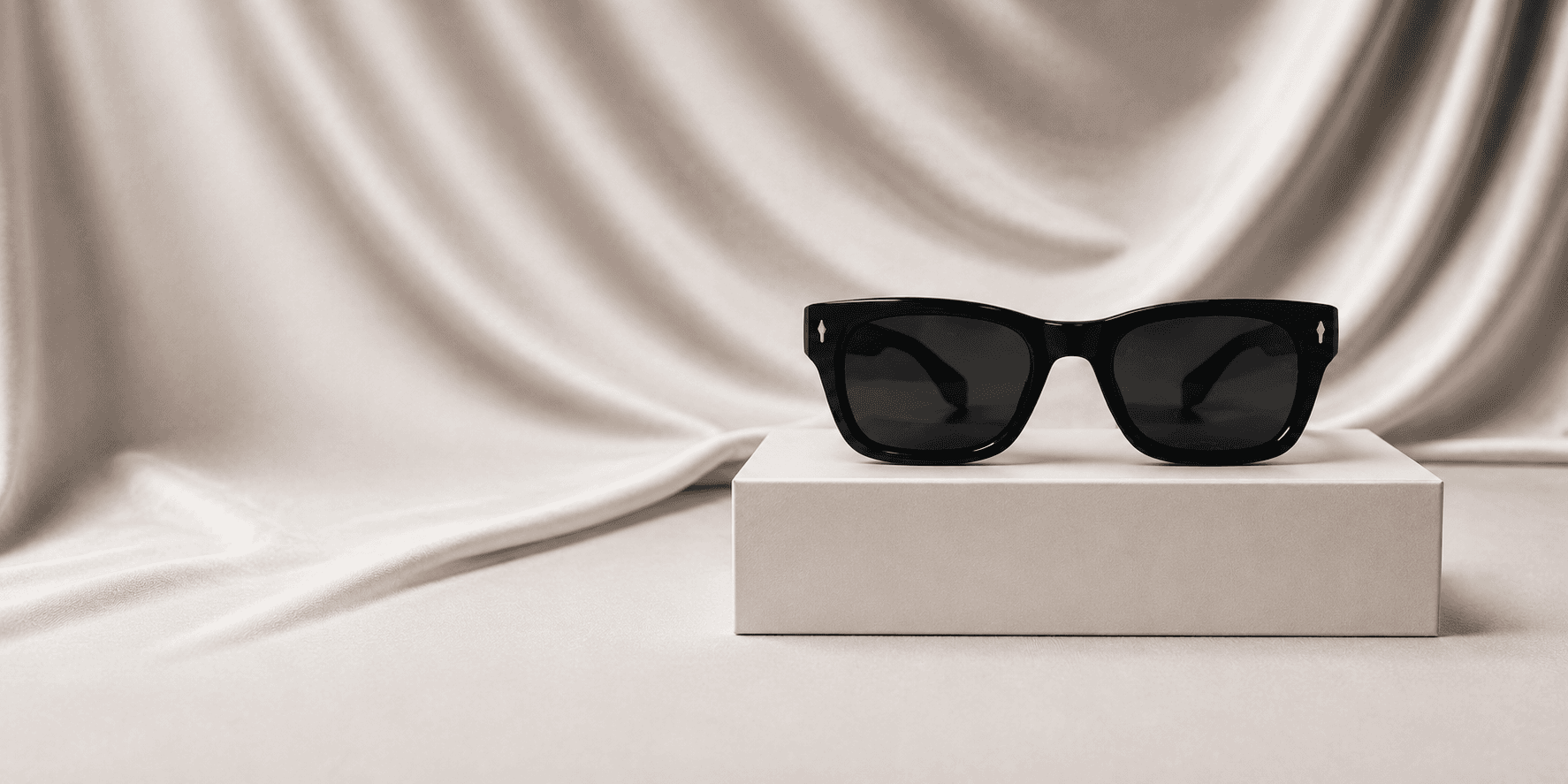 Lunettes de soleil en acétate noir Lumaura posées sur un écrin, tissu drapé en fond